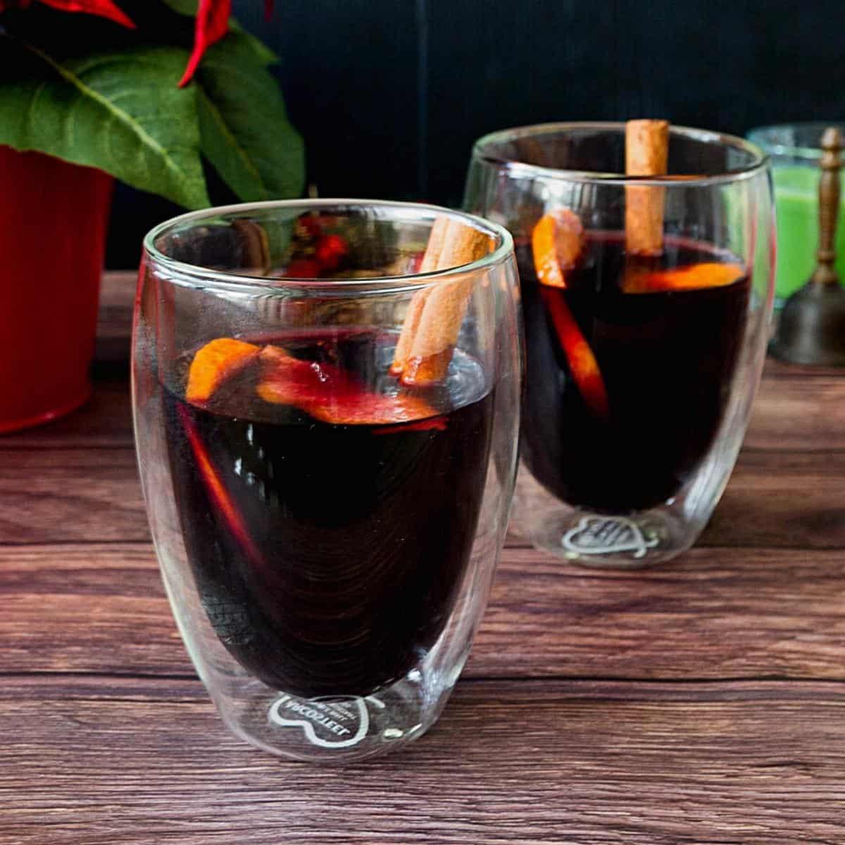 Spiced ginger mulled wine with ruby-red wine, fresh orange slices, and cinnamon sticks in clear mugs.