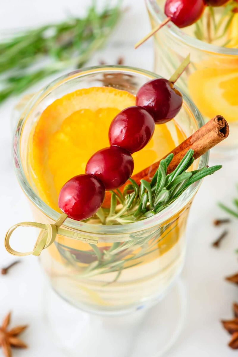 Golden mulled white wine with sliced pears, orange peel, and cinnamon sticks in clear mugs.