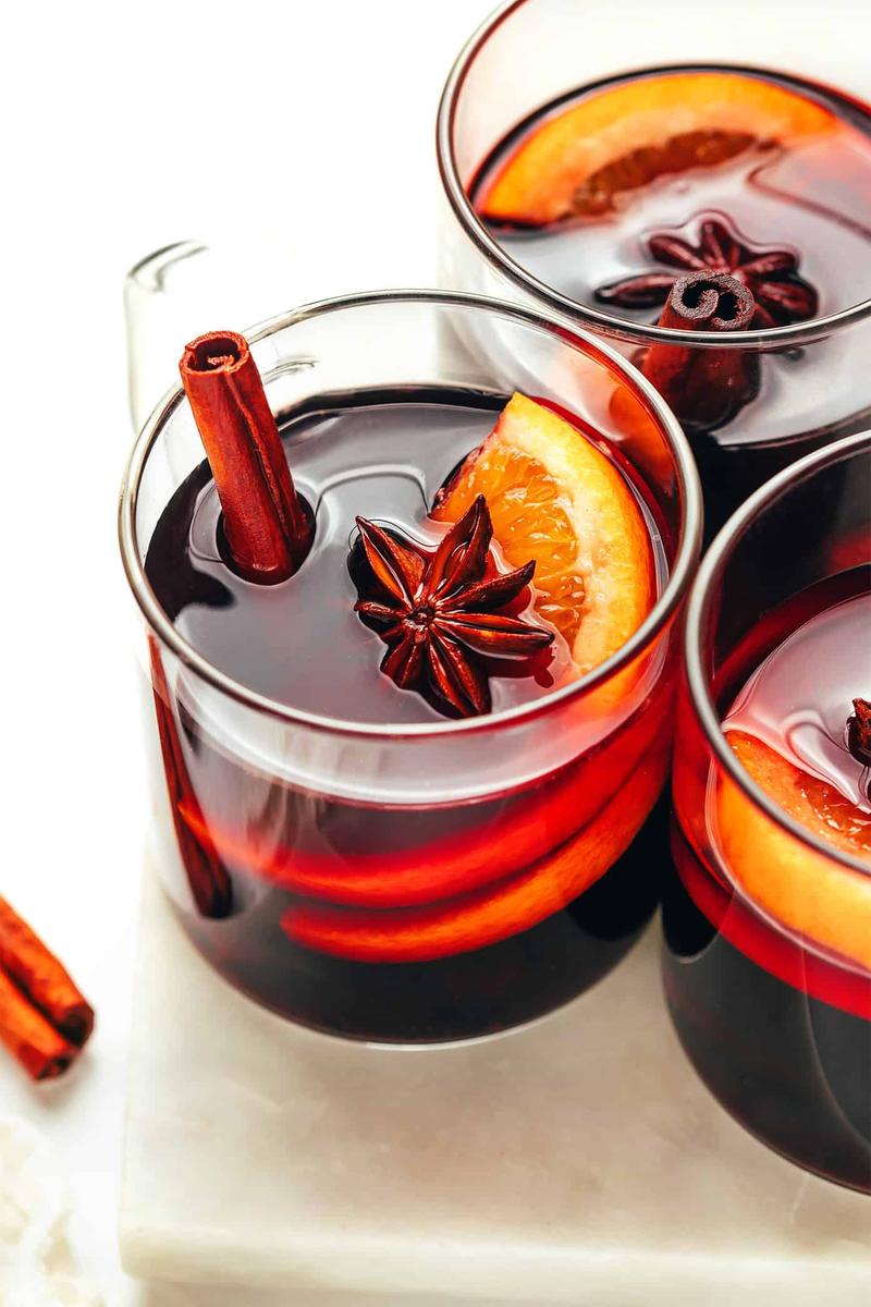 Cherry rosemary mulled wine with dark ruby-red wine, floating orange, and whole cinnamon in mugs.