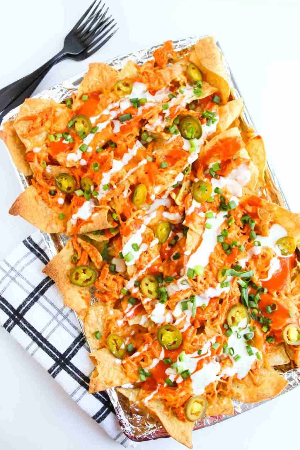 Skillet buffalo chicken nachos featuring melted cheddar, blue cheese, jalapeños, guacamole, and tortilla chips