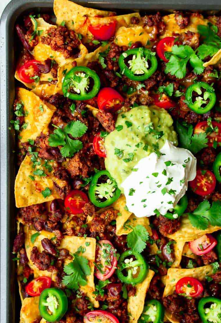 Sheet pan supremo beef nachos layered with melted cheese, refried beans, jalapeños, guacamole, and tortilla chips