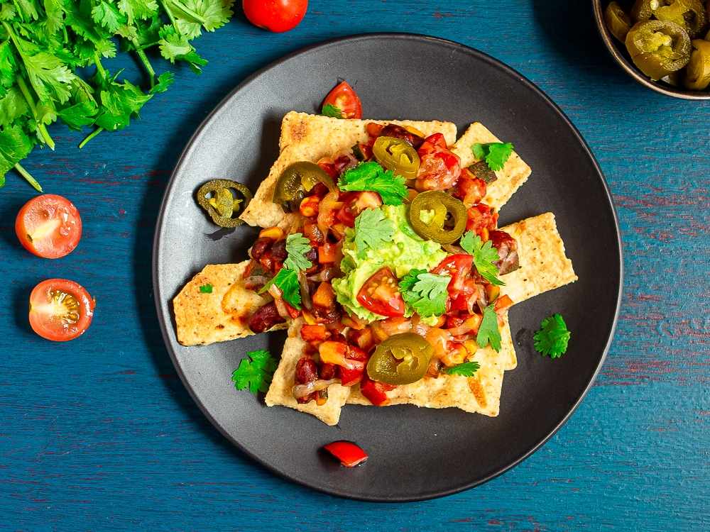 Loaded veggie nachos topped with fresh guacamole, melted jack cheese, black beans, jalapeños, and tortilla chips