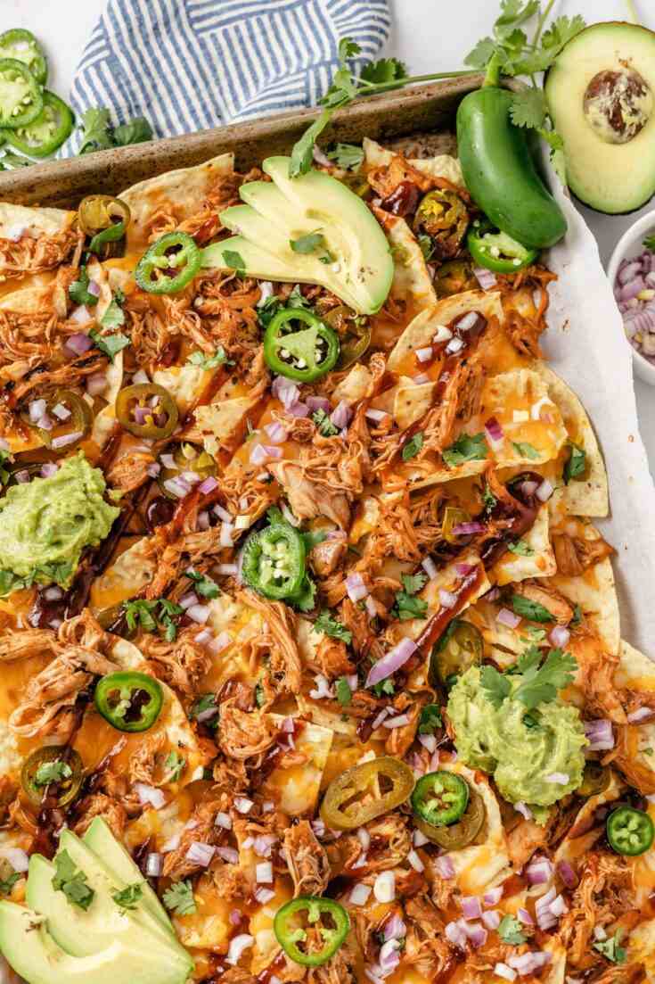 BBQ chicken nachos topped with melted cheddar cheese, pickled jalapeños, guacamole, sour cream, and tortilla chips.