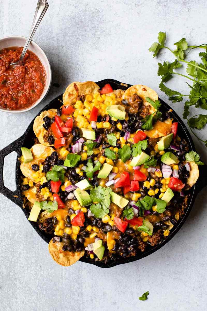Sheet pan nachos with melted queso cheese, sizzling chorizo, jalapeños, guacamole, sour cream, and tortilla chips.