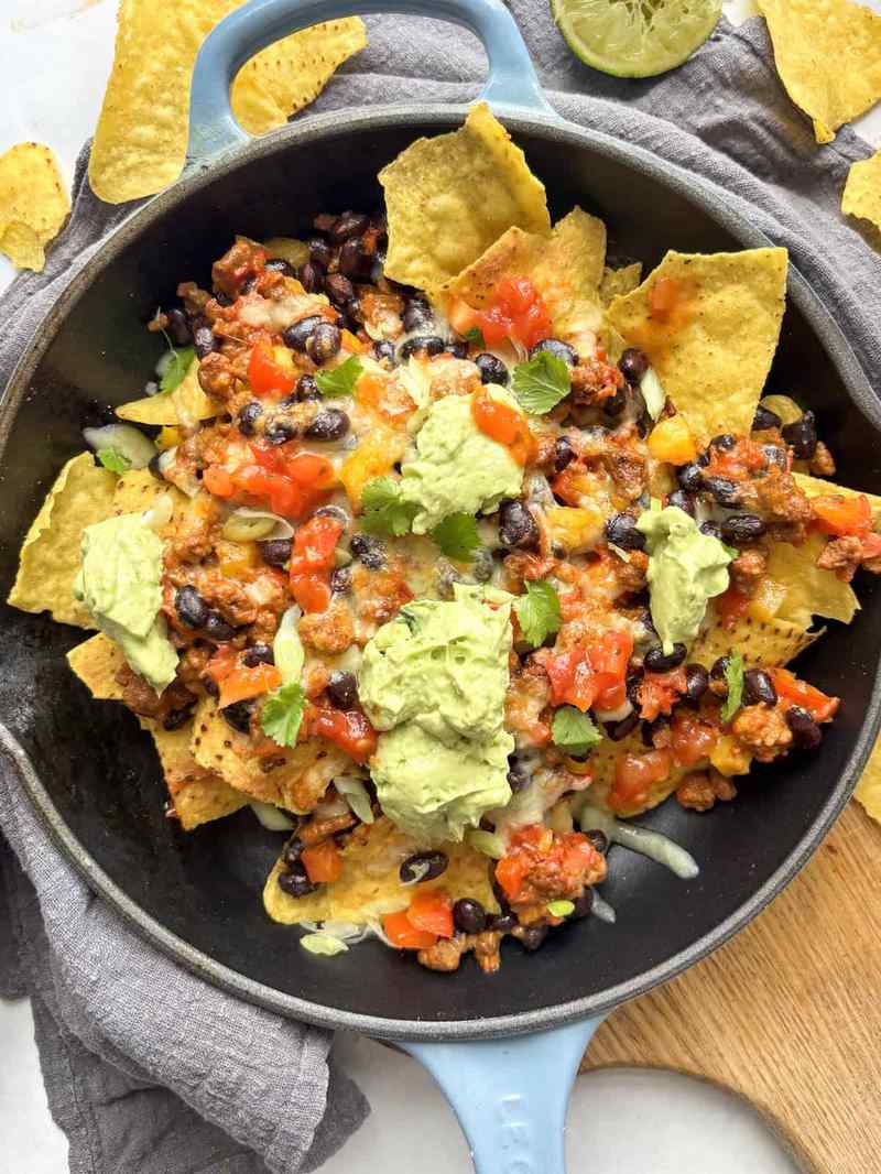 Sheet pan nachos with melted Monterey Jack, jalapeños, shredded chicken, guacamole, sour cream, and tortilla chips.