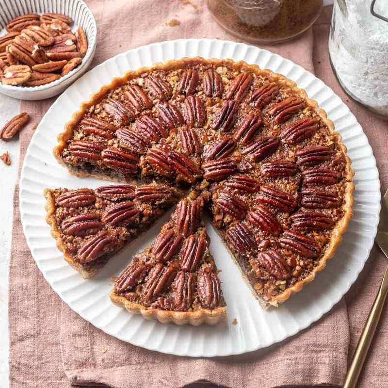 Individual pecan pie tart with toasted pecans and golden caramel filling in flaky pastry crust