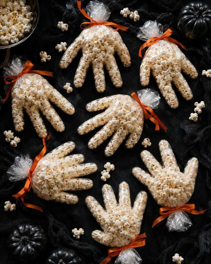 Small paper bags shaped like gloves, filled with caramel‑coated popcorn and orange candy “fingers.”