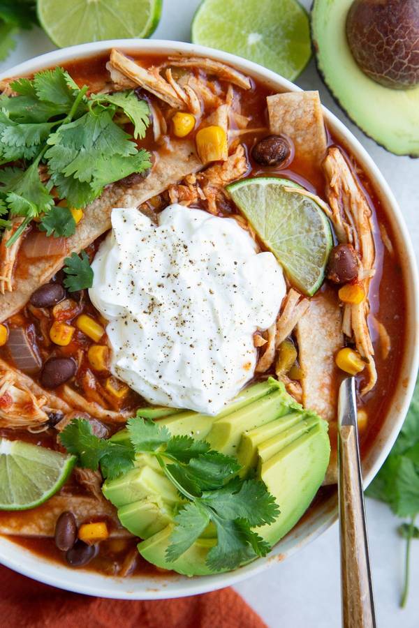 Traditional chicken tortilla soup with tomato broth, shredded chicken, crunchy strips, avocado, lime