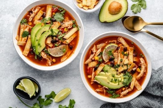 Traditional chicken tortilla soup with tomato broth, shredded chicken, crunchy tortilla strips, avocado, lime