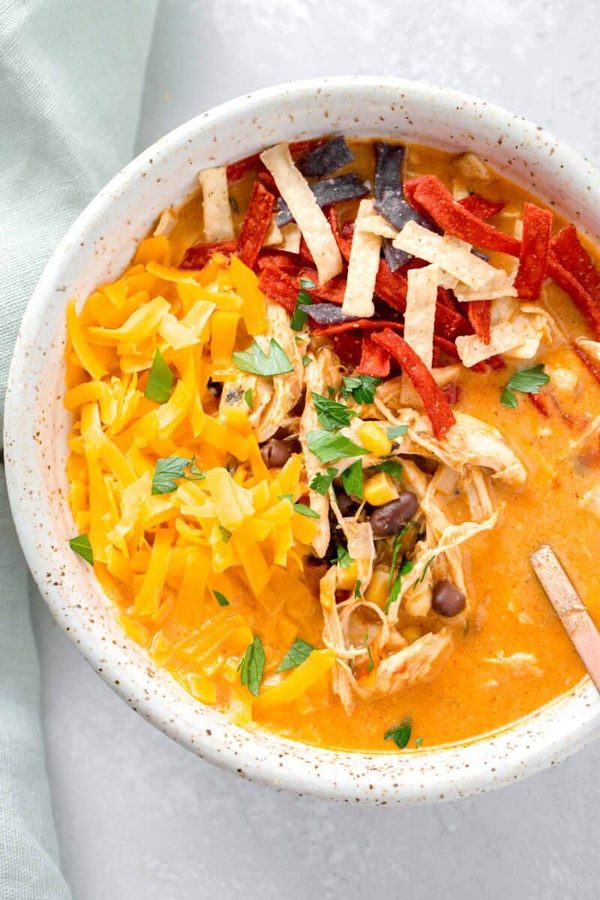 Creamy chicken tortilla soup with roasted red pepper broth, shredded chicken, crunchy tortilla strips, avocado, and lime