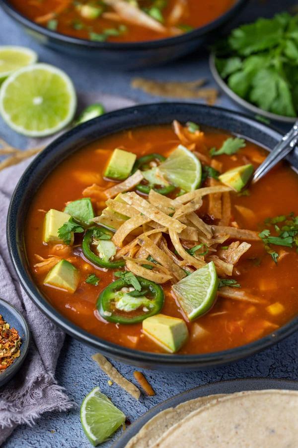 Classic chicken tortilla soup with hearty tomato broth, shredded chicken, crispy tortilla strips, avocado, and lime