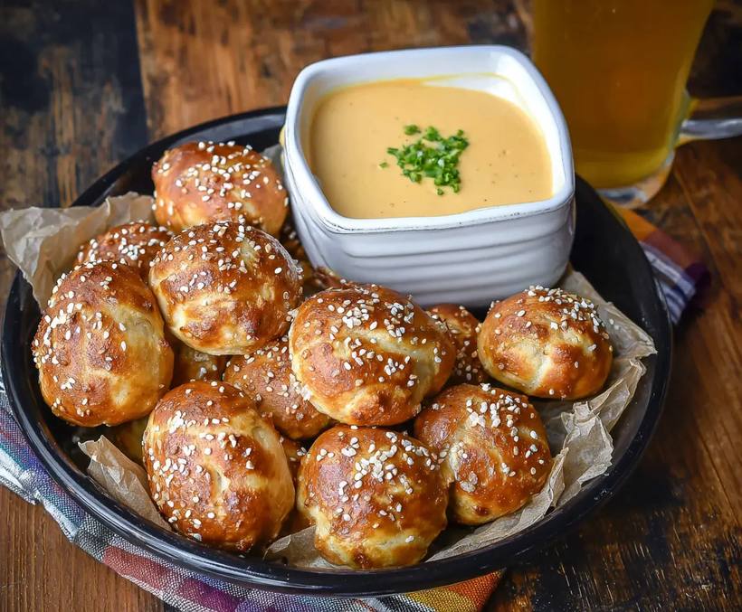 Soft pretzel bites alongside a zesty beer cheese dip, bright orange and creamy