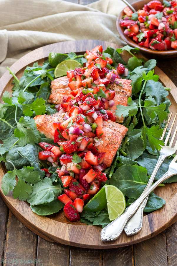 Grilled salmon served with vibrant strawberry salsa, lime wedges, and fresh dill garnish