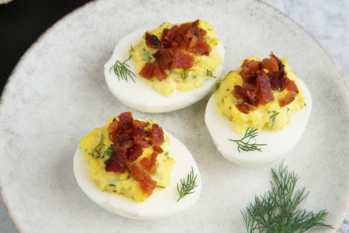 Creamy deviled egg halves topped with crisp bacon and fresh dill sprigs