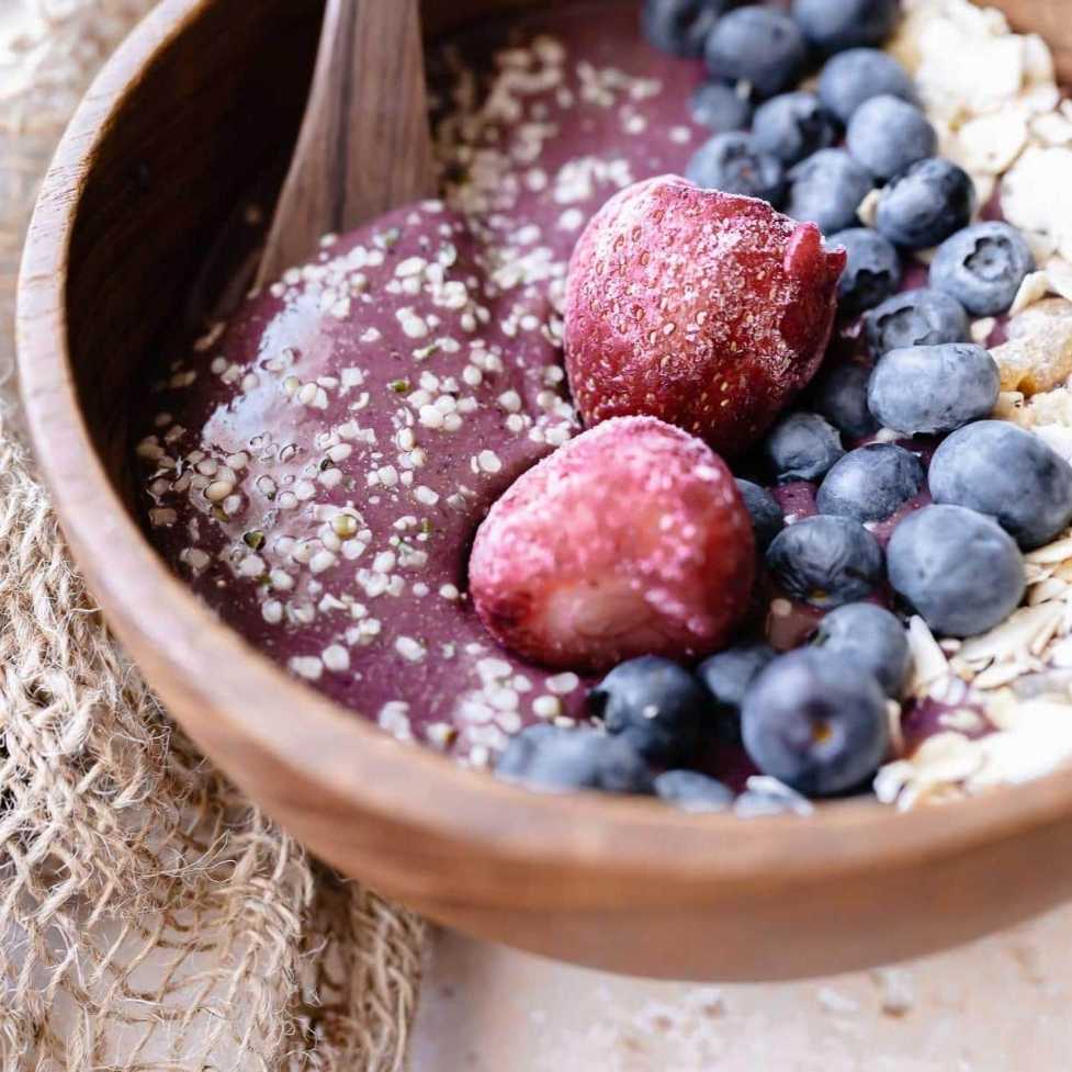 Vibrant purple acai bowl topped with sliced strawberries, blueberries, granola, and coconut flakes in a ceramic bowl.