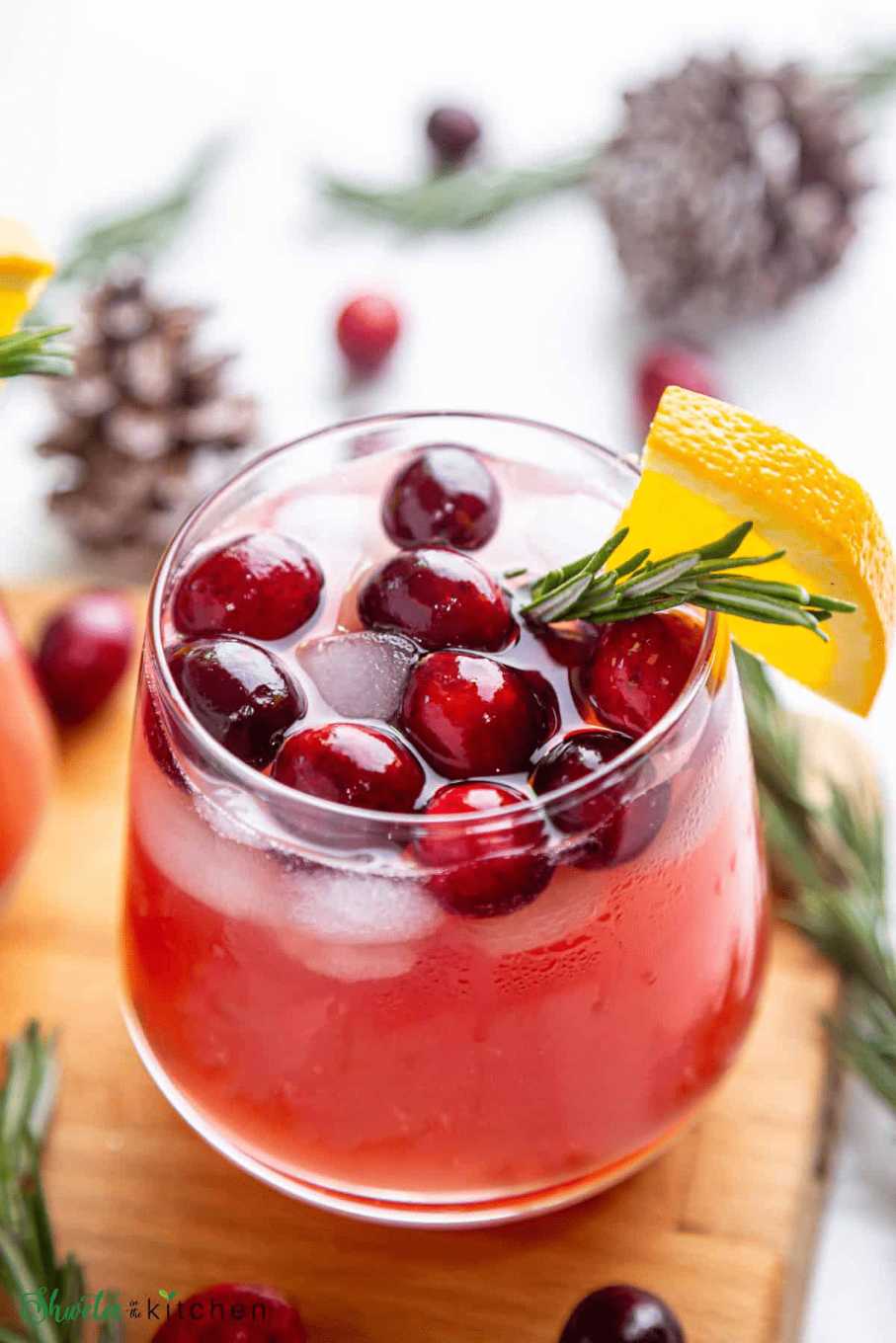 Bright red cocktail in a tall glass with an orange slice garnish and a sprig of rosemary on the rim.