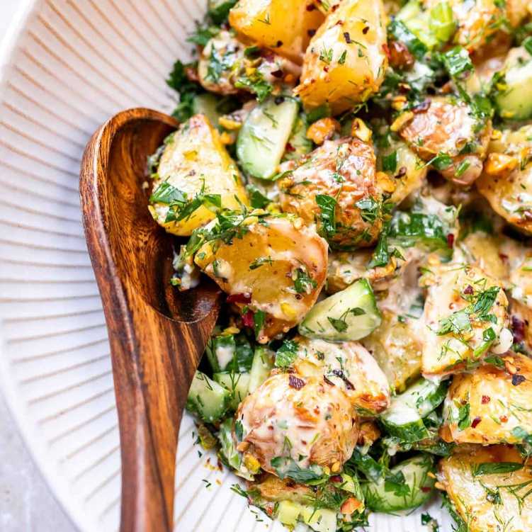 Diced potatoes in a creamy mayo-based dressing with fresh chives, parsley, and celery in a serving bowl.