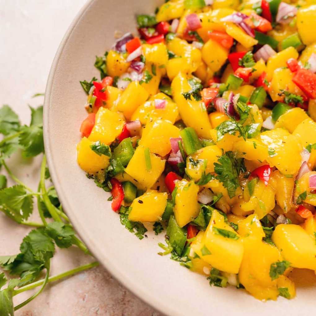 Bright orange and green salsa with diced mango and bell peppers in a bowl with tortilla chips on the side.